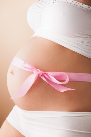 Pregnant belly with pink ribbon. Third trimester.の写真素材