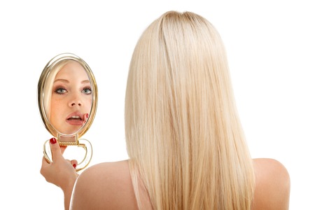 Young woman checking her hair in mirror, isolated at white.の写真素材