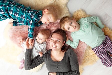 Top view of beautiful young mother, their cute little daughter and two son, lying on wooden floor.