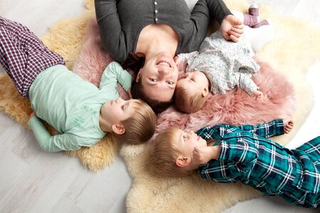 Top view of beautiful young mother, their cute little daughter and two son, looking at camera and smiling, lying on wooden floor.の写真素材