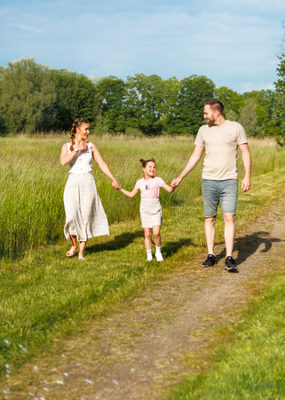 Summer sunny day for a young family, dad, mom and little girl became joyful and happy. Beautiful flower meadow, happy family concept.の写真素材