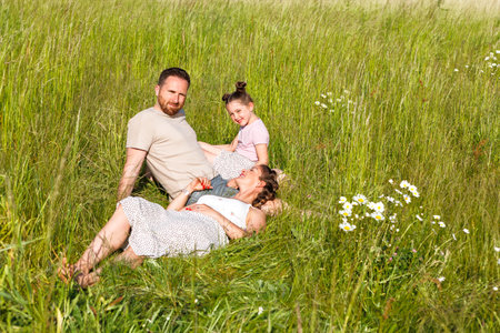 Summer sunny day for a young family, dad, mom and little girl became joyful and happy. Beautiful flower meadow, happy family concept.の写真素材