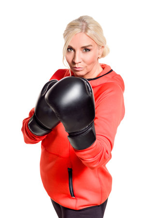 A mature woman wearing boxing gloves and a sporty outfit is ready for a workout. She exudes confidence and strength as she trains, focused on her boxing technique. The bright outfit contrasts with the intensity of the black gloves, highlighting her determination and active lifestyle.の写真素材