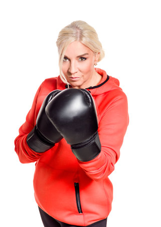 A mature woman wearing boxing gloves and a sporty outfit is ready for a workout. She exudes confidence and strength as she trains, focused on her boxing technique. The bright outfit contrasts with the intensity of the black gloves, highlighting her determination and active lifestyle.の写真素材