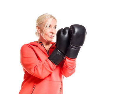 A mature woman wearing boxing gloves and a sporty outfit is ready for a workout. She exudes confidence and strength as she trains, focused on her boxing technique. The bright outfit contrasts with the intensity of the black gloves, highlighting her determination and active lifestyle.の写真素材