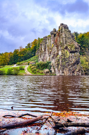 The Externsteine rock columns, standing 40 meters tall, form a striking natural monument in a peaceful nature reserve in Germany. Surrounded by autumnal colors, the reflection of the rocks and foliage create a picturesque scene on the lake.の写真素材
