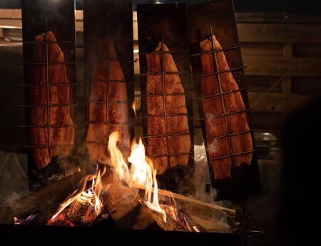 smoked fish fried over open fire with burning firewood in the nightの写真素材