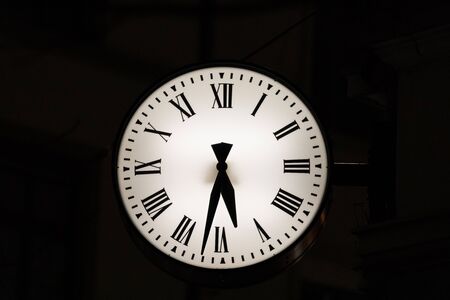 white old antique luminous clock with hour and minute hands in front of black backgroundの写真素材