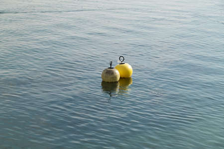 two water buoys floating in the water one white the other yellow plastic remains hang on the yellow buoy during the day in good weather without peopleの写真素材