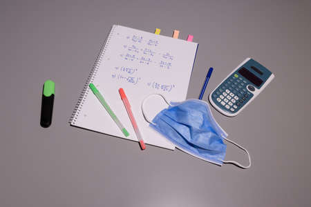 blue protective mask against the corona virus Covid 19 on a gray table, mathematics notebook with colored pens, calculator, the medical masks must be worn by young people in class to prevent infections that can cause serious health problemsの写真素材