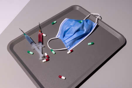 corona covid 19 protective mask on a medical drug instruments tray on a gray table with vaccine...