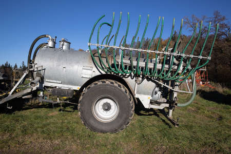 silver manure wagon without tractor with green hoses standing on an autumn meadow in the morning,...