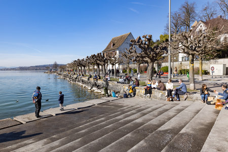 rapperswil jona, sankt gallen, switzerland - february 20, 2021: beach promenade, many people enjoy the warm sun by the water after the long lockdown, by dayのeditorial素材