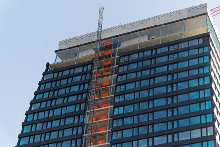 basel switzerland april 24. 2021: blue skyscraper with red construction and scaffold lift in front of cloudless sky, in big cities more and more construction is going on, during the day without peopleのeditorial素材