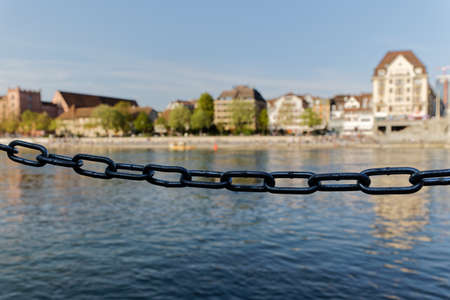 metal barrier chain in shadow in front of blue river and house facade, strong focus on the metal...
