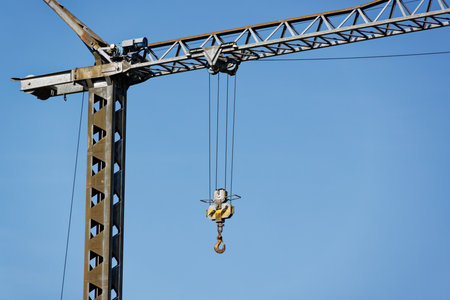 gray construction crane with big pick to lift and move elements in front of blue sky, construction...