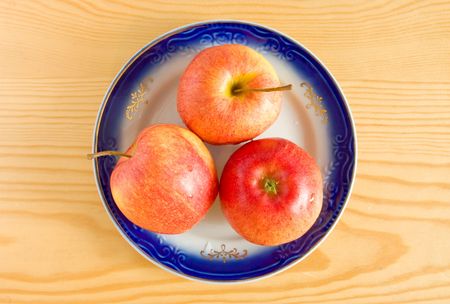 Three apples on plate at wood backgroundの写真素材