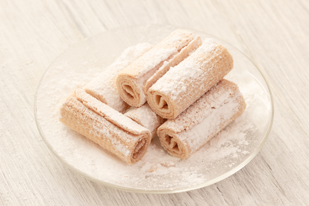 Crunchy sweet waffle rolls on plate with sugar powderの写真素材
