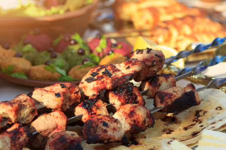 Spicy pork meat grilled on fire (traditional shashlik) with other foods on event served table, selective focusの写真素材