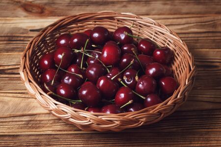 Dark red sweet cherry in wicker plate in rustic style on wooden table closeupの写真素材