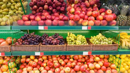 Supermarket shelves with fruits. Apples, grapes and other sweet fruits selling on showcaseの写真素材