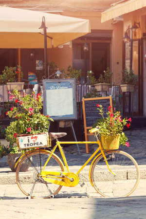 Tropea, Italy - September 5, 2019: Decorative flowers pot on bicycle near the restaurant on Tropea town street. Vintage yellow bicycle symbol with I love Tropea caption and bloom flowers decorationのeditorial素材