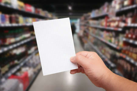 Paper for shopping list in hand at blurred background with supermarket aisleの写真素材