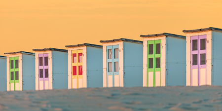 Panoramic image of a row of old colorful wooden beach cabins during sunsetの写真素材