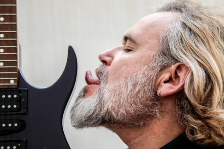 A Blonde Long Haired Bearded Man Licking His Electric Guitar