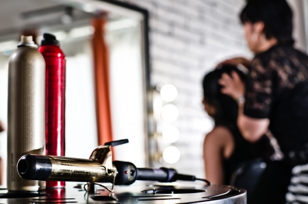 Hairspray and curling iron on the bottom left of the frame and the stylist and client blurred in the backgroundの写真素材
