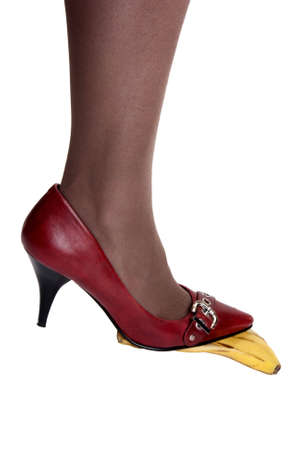 Foot in red pumps on banana peel against a white backgroundの写真素材