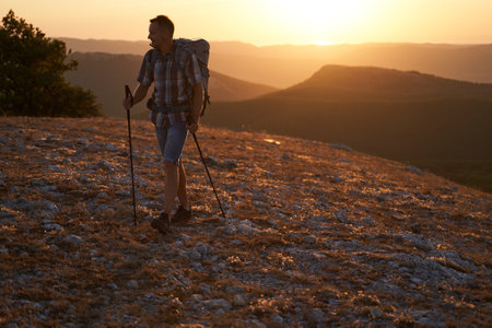 Hike mountain man hiking travel with backpack and trekking poles walking at adventure and sunset. High quality photo.の写真素材
