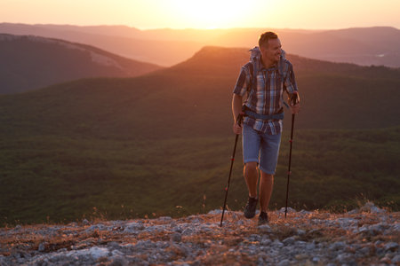 Young hiker with backpack and trekking poles walking along a crimea mountain path at sunset with a smile. High quality photo.の写真素材