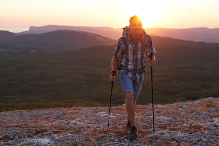 Hike mountain man hiking travel with backpack and trekking poles walking at adventure and sunset. High quality photo.の写真素材