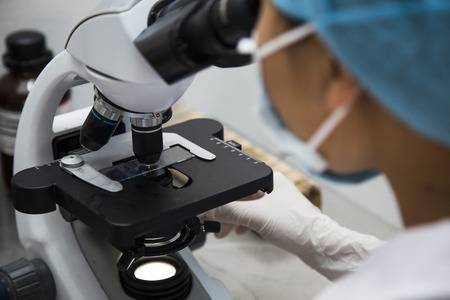 Serious Asian clinician studying chemical element in laboratory, focus on the microscopeの写真素材