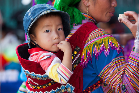 Lao Cai, Vietnam - Oct 17, 2015: A little Hmong (Miao) child on his mother back coming down to town to attend the weekly traditional outdoor market in Bac Ha district, north west of Vietnam.のeditorial素材