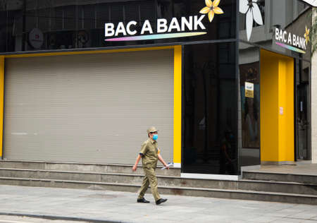 Hanoi, Vietnam - Mar 28, 2020: A volunteer security guard man with face mask walking pass a Vietnamese local bank office closes on weekend to prevent the Corona Virus (Covid-19) spreading.のeditorial素材