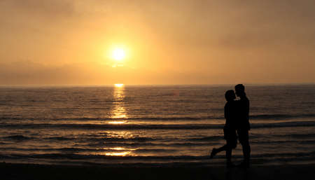 Lovers on the beach at sunset. happy Couple Kissing and hugging in Front Of Sun and sea waves. Romantic Lover Concept.の写真素材