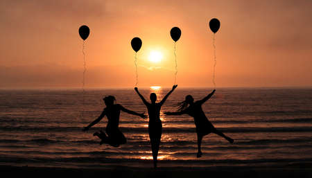 Silhouettes Of Happy Girls Jumping On the Sunset Beach Enjoying life Together With Party Balloons. Holidays and Happiness concept ideaの写真素材