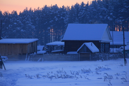 Country house on the background of a winter forest and sunsetの写真素材