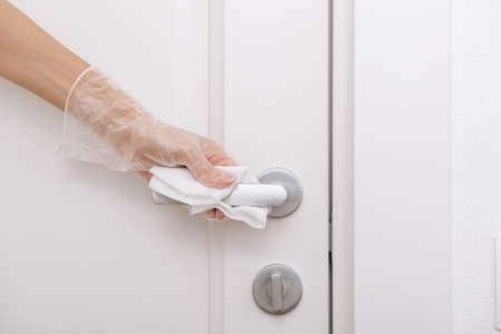 Cleaning door handles with wet wipe and white gloves. Sanitize surfaces prevention in hospital and public spaces against  virus. Woman hand using towel for cleaning home room door link.の写真素材
