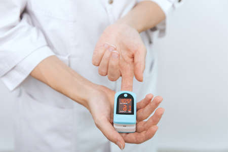 Pulse oximeter with hand of doctor isolated on white. Measuring oxygen saturation, pulse rate and oxygen levels. The concept of portable digital device to measure persons oxygen saturation.の写真素材