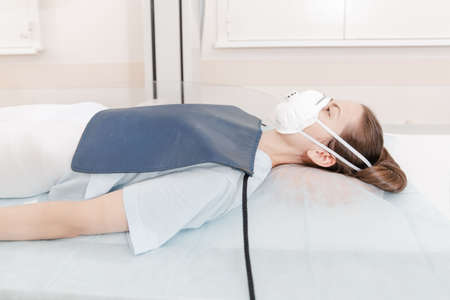 Doctor taking x-ray of patient lying on gurney. Hospital radiology room. Technician adjusting an x-ray machine. Female lying on a bed is scanning chest, heart, lungs in modern clinic office.の写真素材