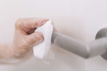 Cleaning door handles with wet wipe and white gloves. Sanitize surfaces prevention in hospital and public spaces against corona virus. Woman hand using towel for cleaning home room door link.の写真素材