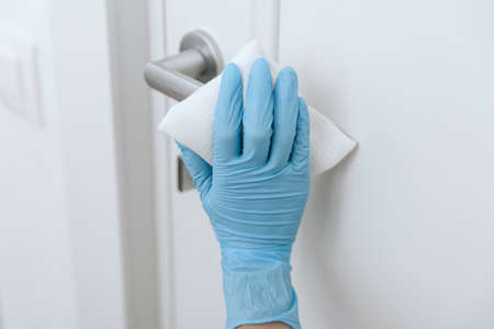 Cleaning black door handles with an antiseptic wet wipe and blue gloves. Sanitize surfaces...