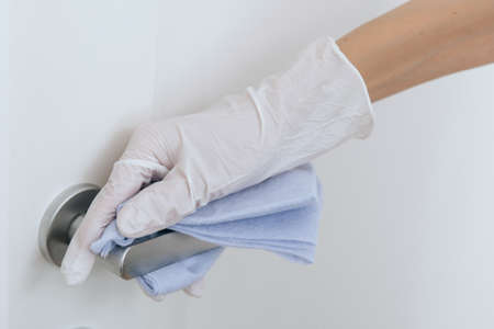 Cleaning door handle with blue wipe in white gloves. Sanitize surfaces prevention in hospital and public spaces against corona virus. Woman hand using towel for cleaning home room door link.の写真素材