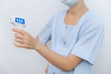 Temperature measurement gun in doctor hands. Close-up shot of doctor wearing protective surgical...
