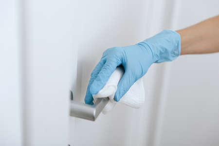 Cleaning black door handles with an antiseptic wet wipe and blue gloves. Sanitize surfaces prevention in hospital and public spaces against corona virus. Woman hand using towel for cleaning.の写真素材