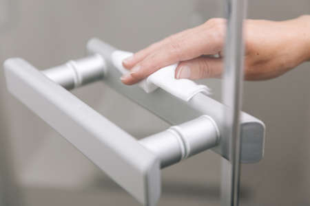 Cleaning glass door handles with an antiseptic wet wipe. Sanitize surfaces prevention