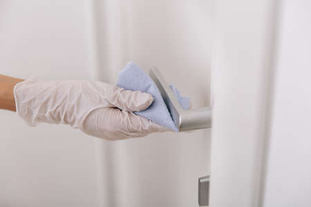 Cleaning door handle with blue wipe in white gloves. Sanitize surfaces prevention in hospital and public spacesの写真素材
